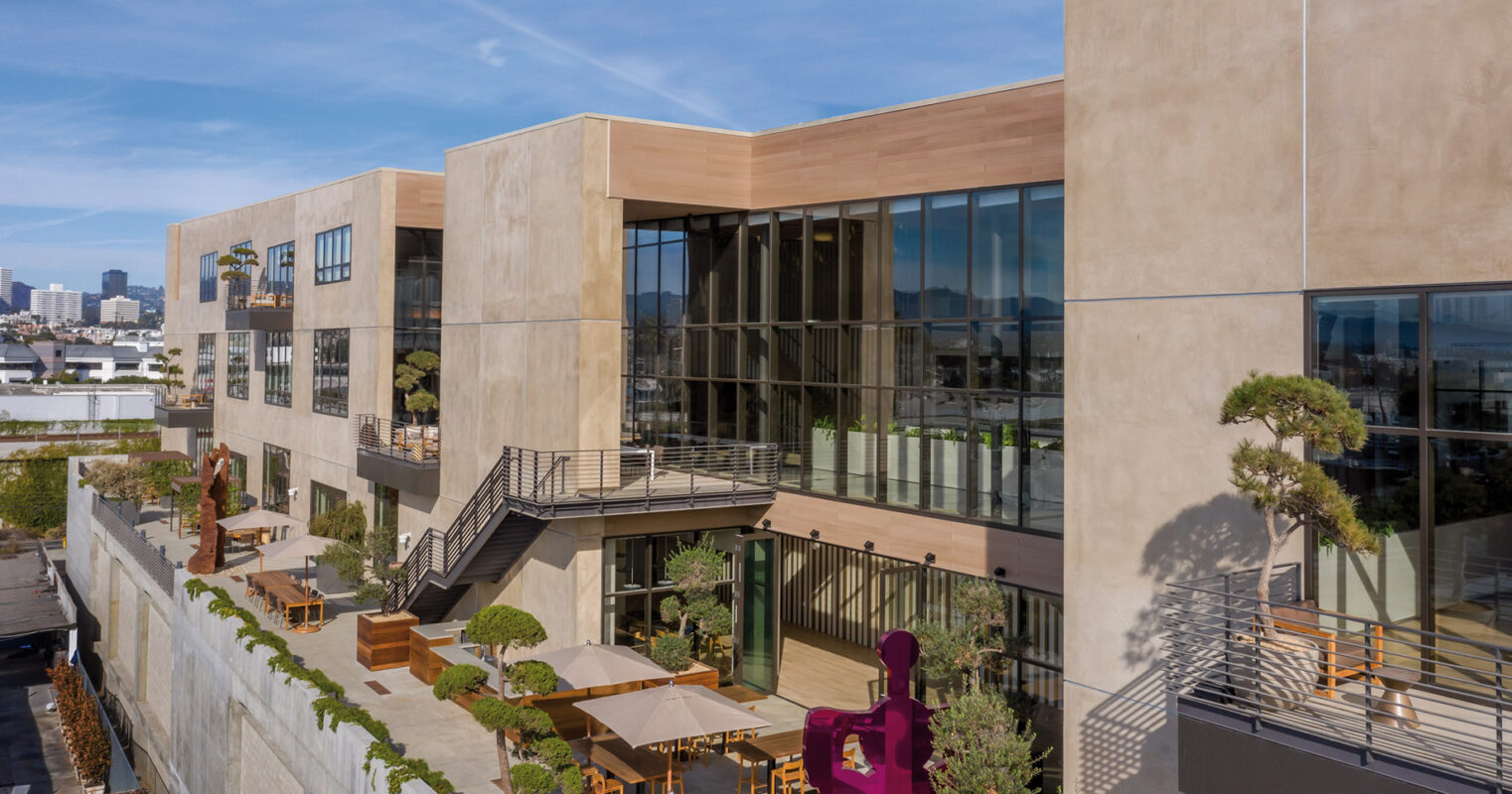 Modern urban building with a rooftop garden and outdoor seating area, showcasing sustainable architecture in a cityscape.