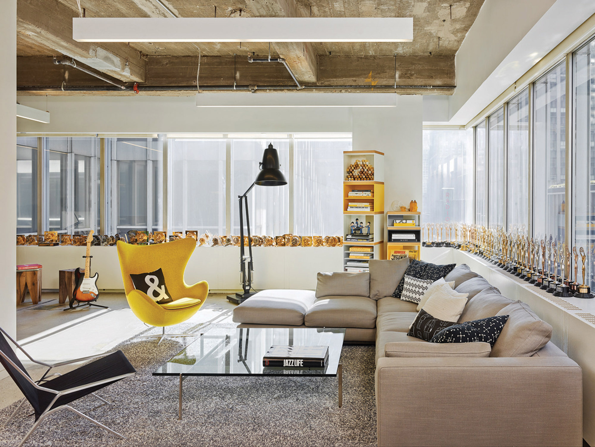 Bright corner lounge with trophy-filled shelves, large windows, and a vibrant yellow accent chair adding a pop of color.