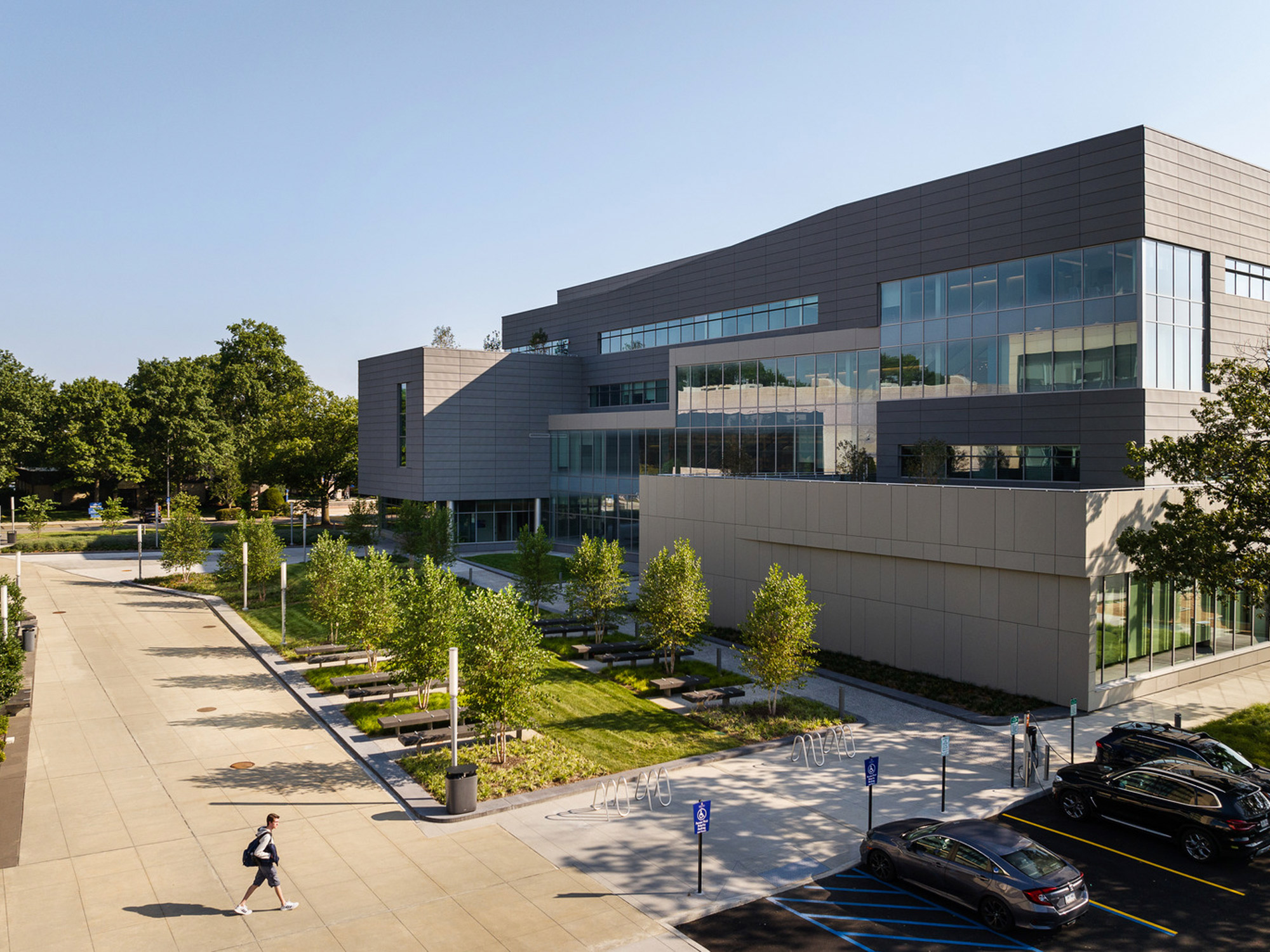 Modern educational building with a sleek design featuring expansive windows and a landscaped approach, with students and visitors making their way along the accessible pathways on a sunny day.