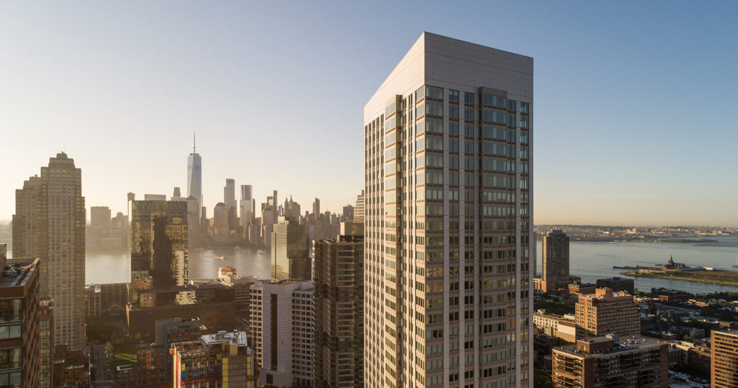 A cityscape at sunset, featuring a mix of modern and traditional skyscrapers against a clear sky, with a prominent river and distant horizon showcasing an iconic urban skyline.