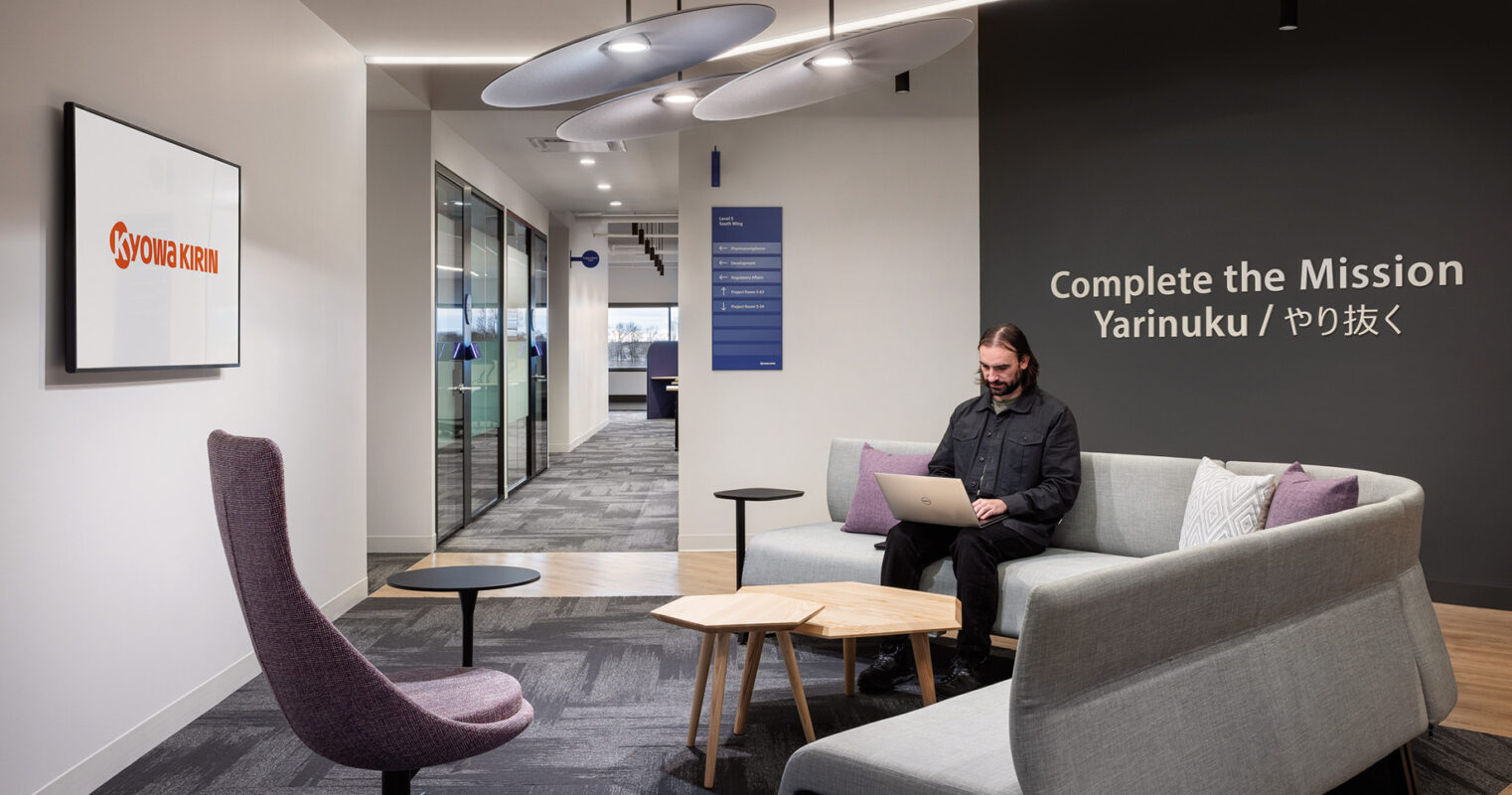 A focused individual working on a laptop in a modern office lounge area with stylish furnishings and corporate branding on the walls.