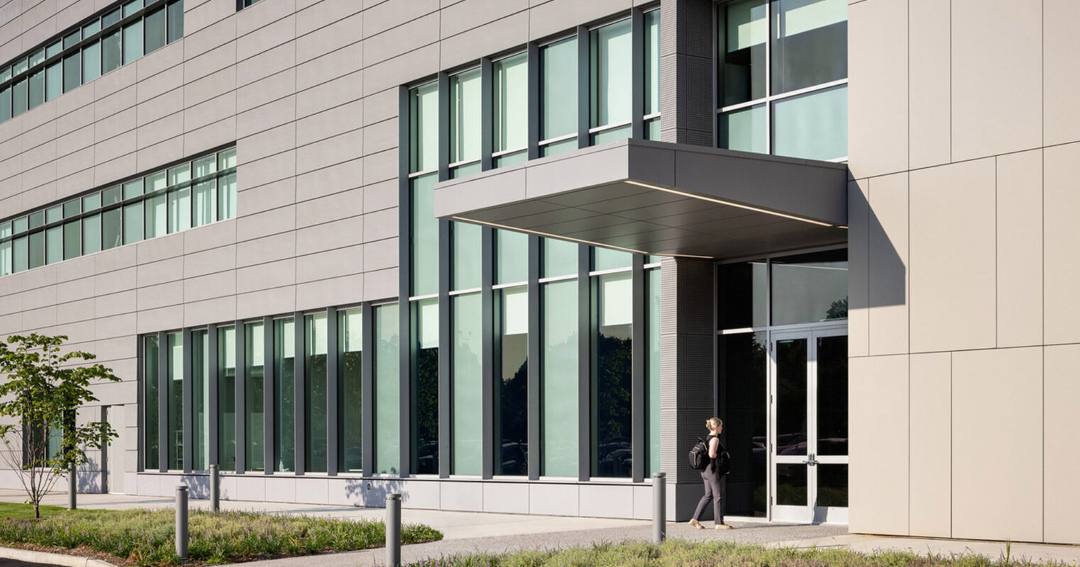 Modern architectural building with a sleek facade featuring symmetrical rectangular windows and an understated canopy entrance. Landscaped with low-lying shrubs and grasses complementing the building's minimalist style.