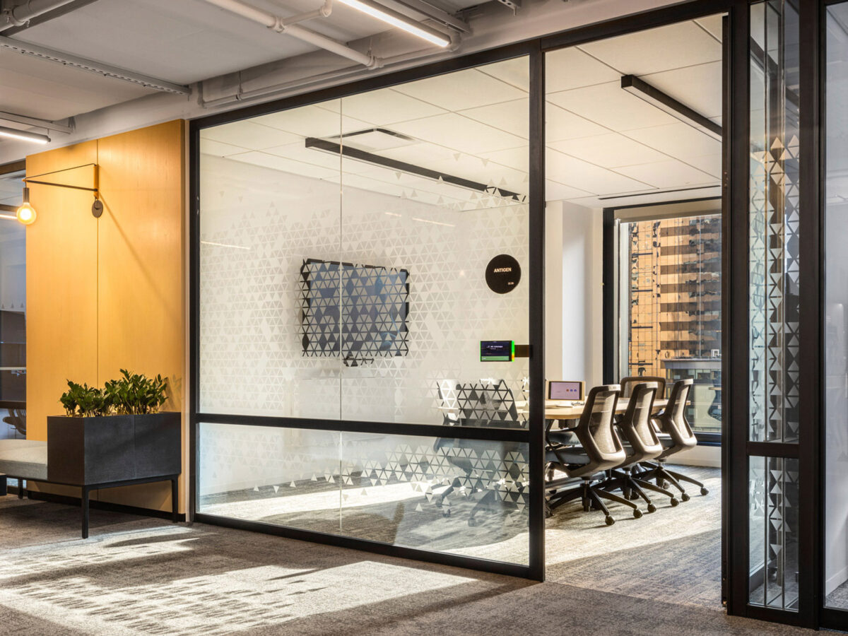 Modern office interior boasting floor-to-ceiling glass walls with geometric frosting patterns, sleek furniture with clean lines, and ambient lighting, creating a transparent, light-filled meeting space embraced by the cityscape outside.