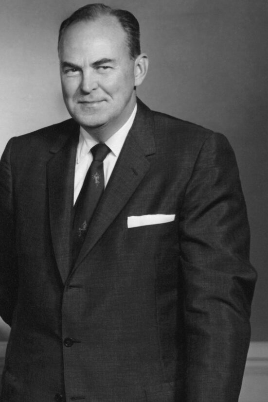 1958 portrait of Charles Haines in a suit with a quiet smile and gazing out to the side.