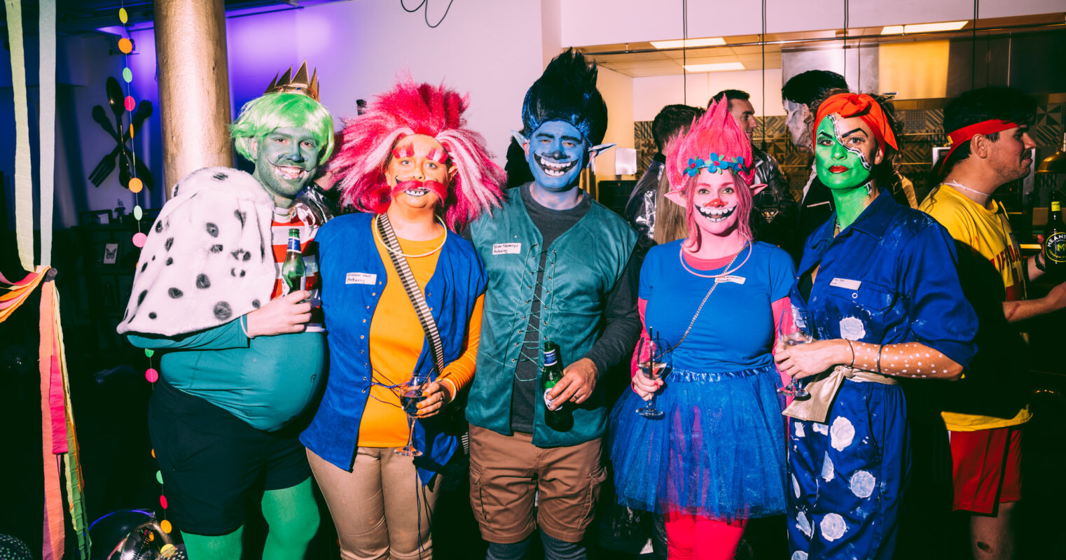 A group of people in colorful, whimsical costumes with face paint and props, enjoying a themed party.