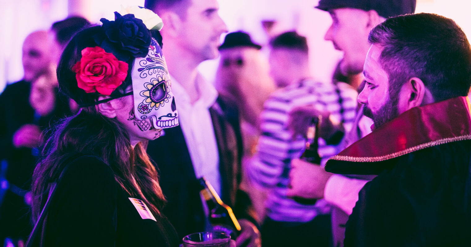 A close-up of a guest in a detailed skull mask, engaging in conversation at a festive event.