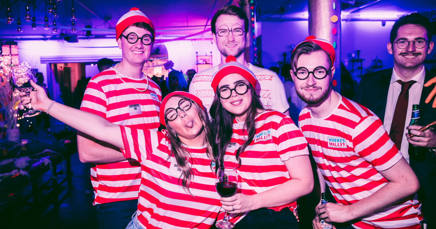 A group in striped shirts and hats playfully impersonates the character Wally from a popular search-and-find book series.