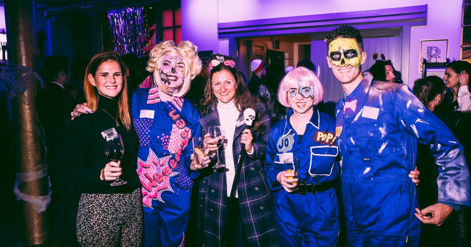A festive gathering of party-goers in face paint and costumes, with drinks in hand.