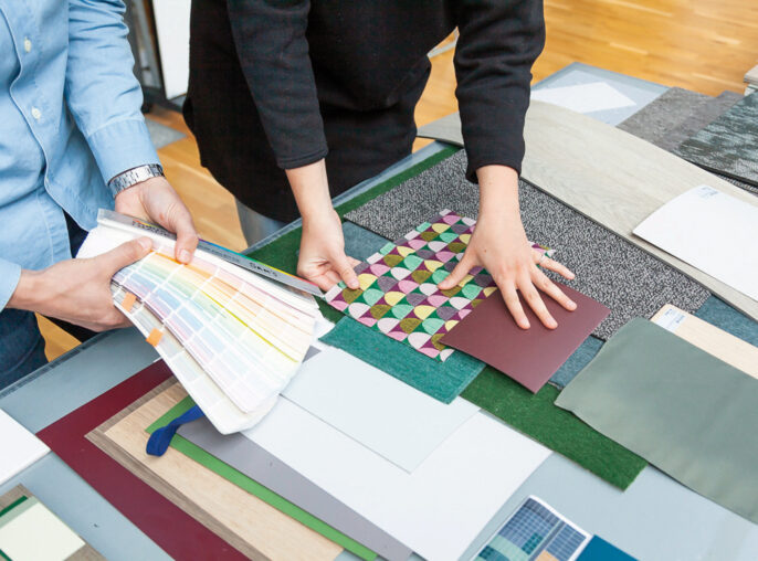 Designers collaborate on a materials board, comparing fabric swatches, color palettes, and flooring samples to craft a cohesive interior design scheme, focusing on texture, color harmony, and sustainable materials.