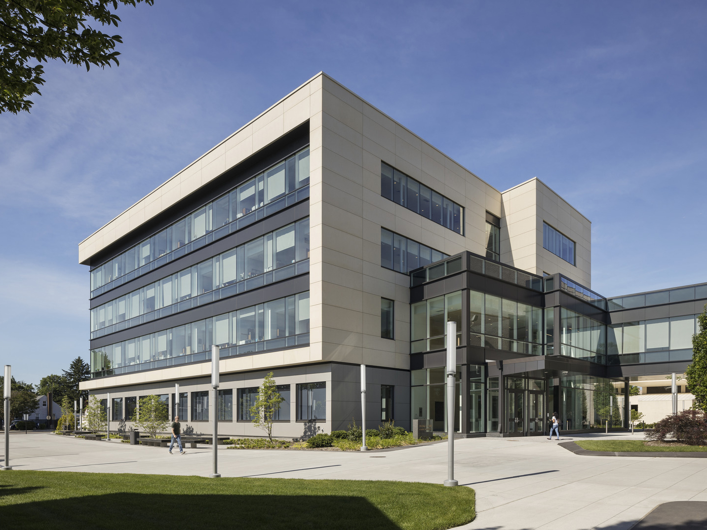 Modern three-story commercial building with an asymmetric facade, featuring a combination of reflective glass windows and pale stone cladding. The ground level’s expansive glazing enhances the indoor-outdoor connection, set against landscaped surroundings.