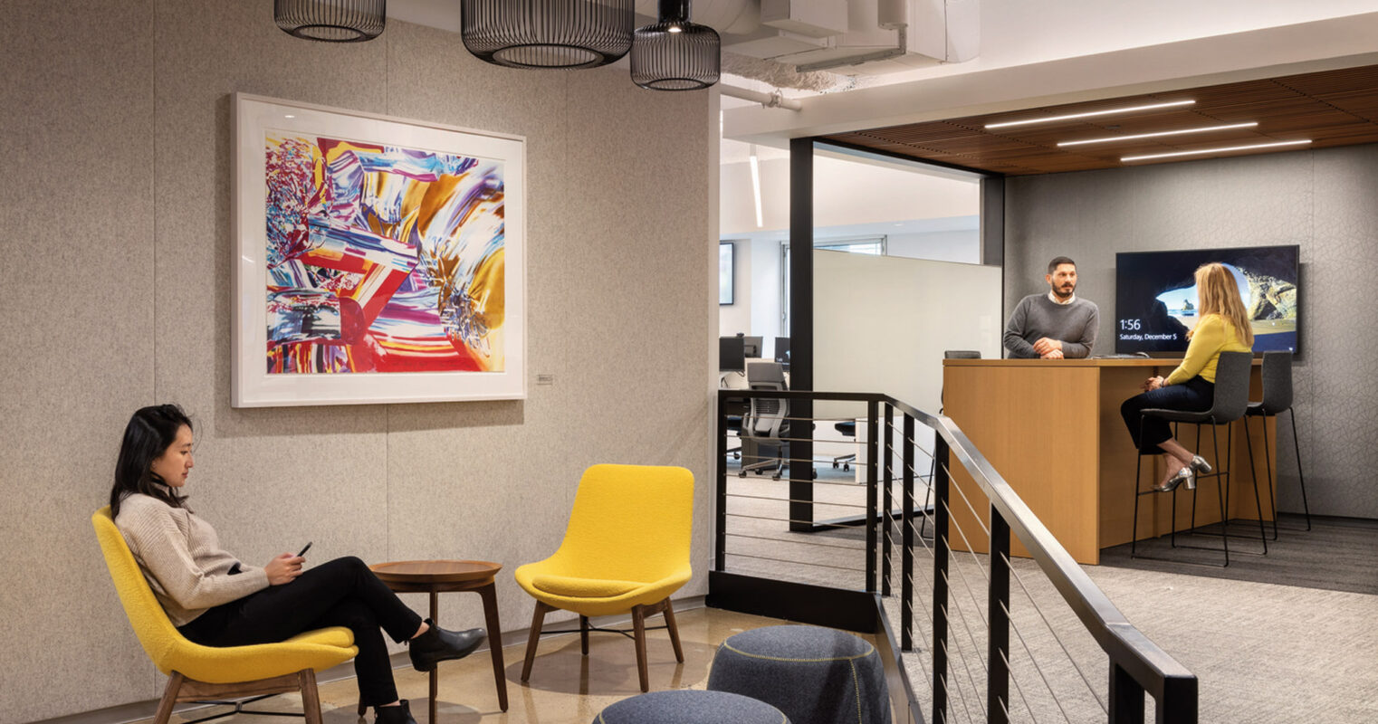 Modern office lobby featuring a minimalist reception desk with a subdued color palette, complemented by vibrant yellow armchairs and a vivid abstract painting, creating a welcoming contrast. Geometric pendant lights and exposed ceiling elements add an industrial touch to the space.