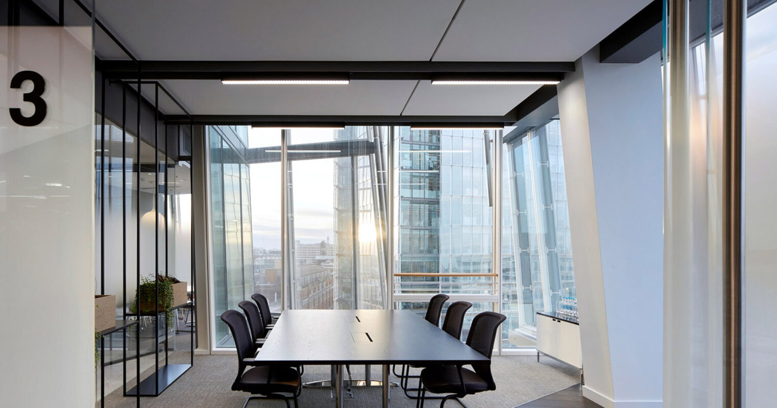 Modern conference room featuring a large, rectangular table with black chairs, expansive windows with city views, sleek overhead lighting, and glass partition walls enhancing an open, airy atmosphere.