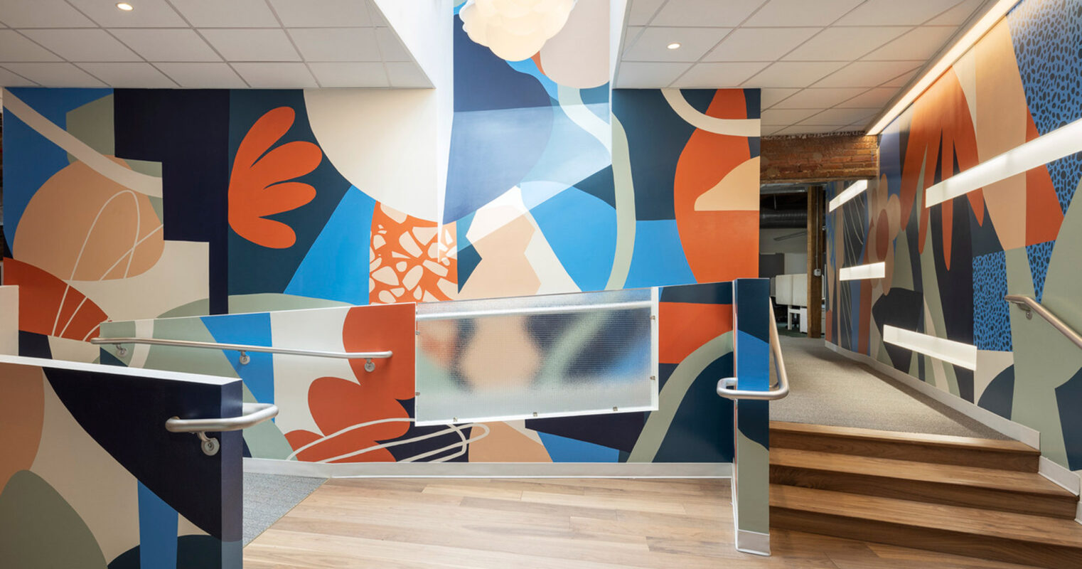 Vibrant mural adorning the walls of a staircase landing, featuring abstract human figures in orange, blue, and gray tones. Warm wooden flooring enhances the modern feel alongside the sleek metal handrails.