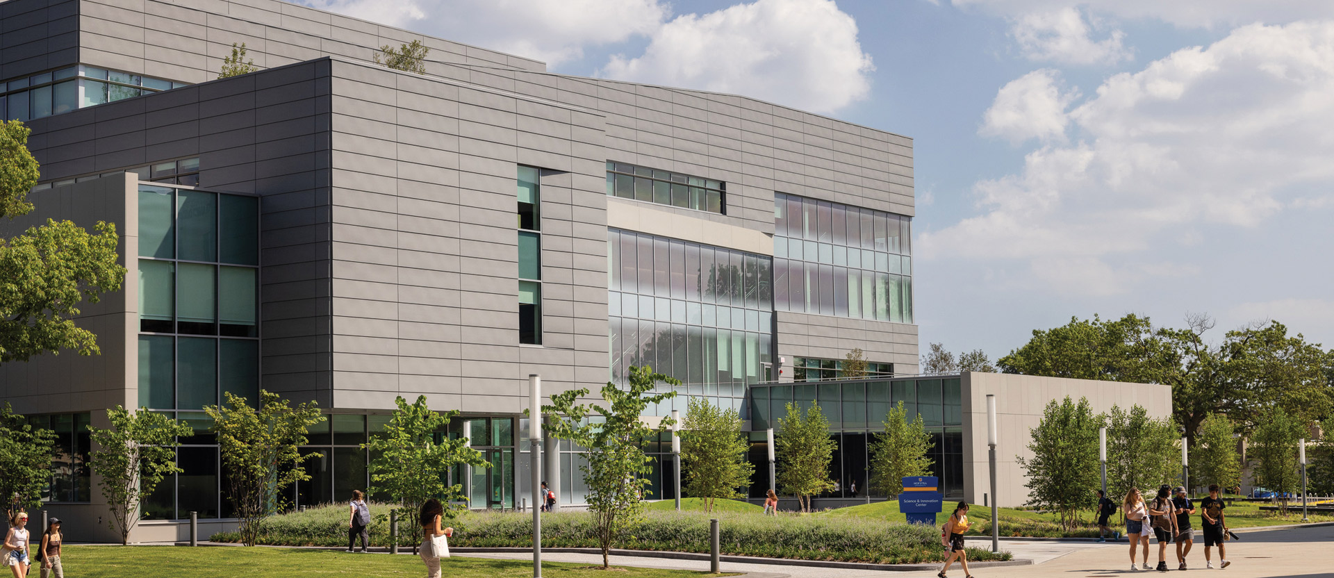 Modern educational building featuring clean lines, expansive glass facade for natural lighting, and aluminum composite panels. Landscaped with young trees and pedestrian pathways, the design encourages student engagement and environmental harmony.