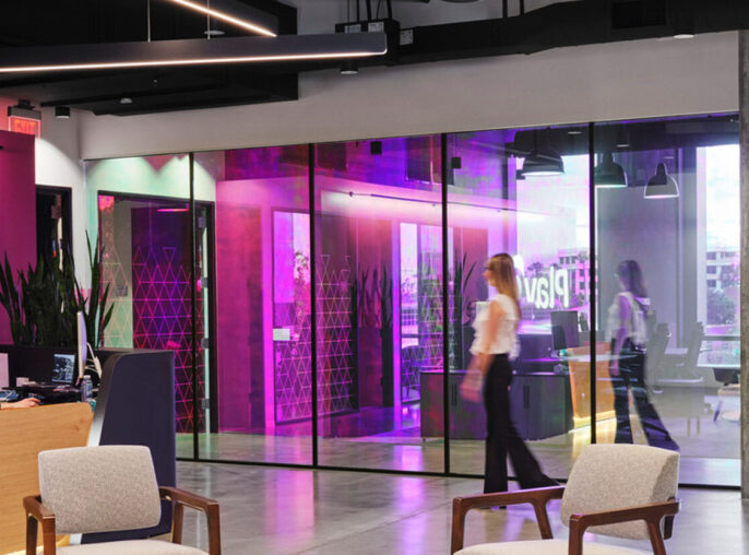 Modern office lobby with a minimalist reception desk, flanked by two white chairs. Vibrant magenta glass panels create a dynamic backdrop, while sleek, geometric light fixtures add a contemporary touch overhead. The design fosters an airy and welcoming atmosphere.