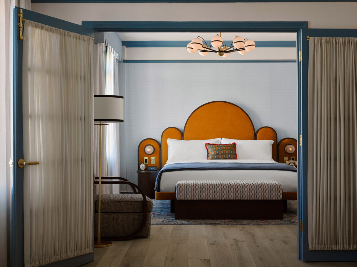 Contemporary bedroom featuring a mustard-hued, scalloped-edge headboard, sky-blue canopy framing, and complementary earth-toned bedding. Art Deco-inspired lighting and furniture accents underscore the room’s elegant aesthetic.