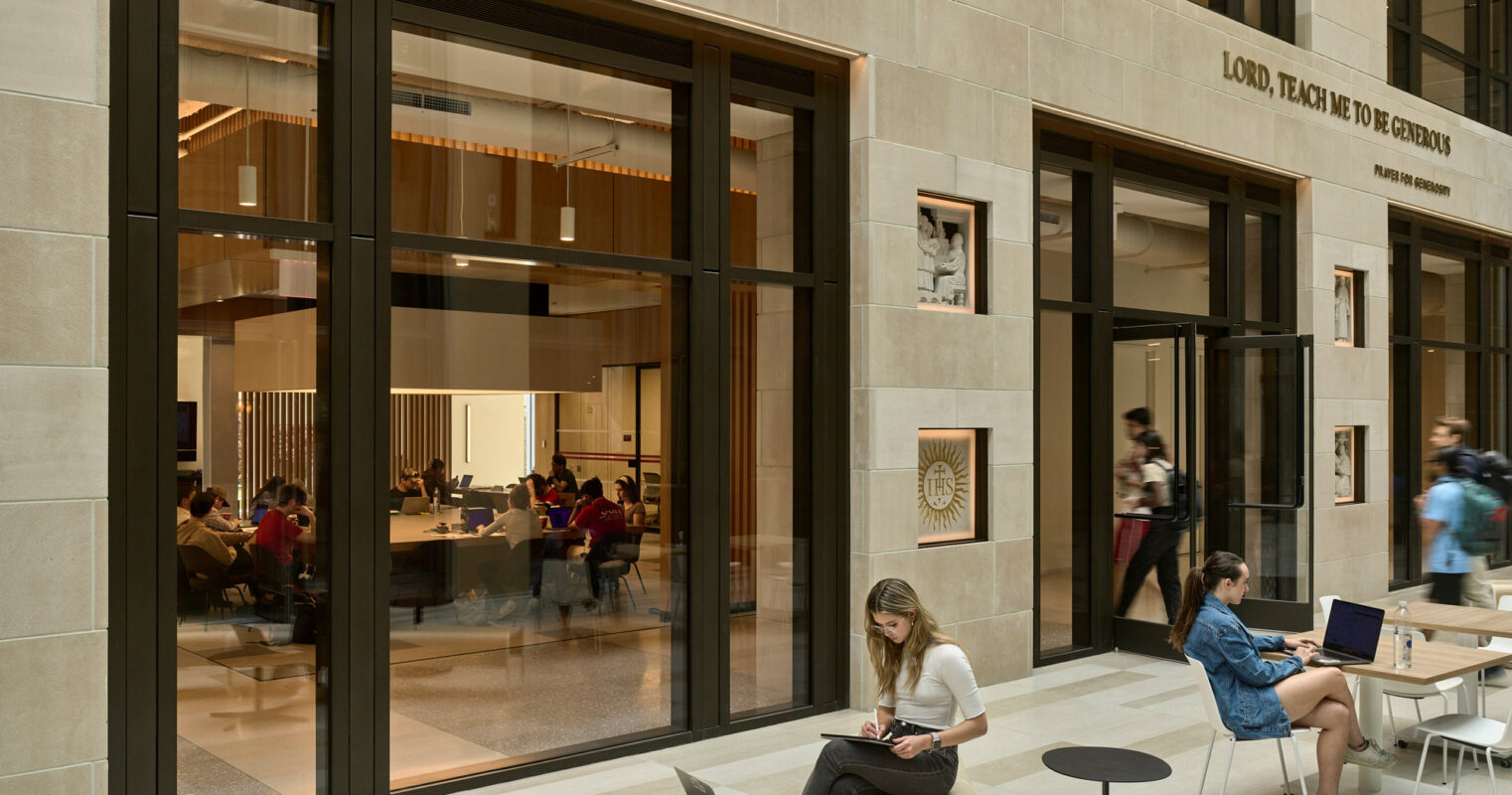 Contemporary educational space blends functionality with aesthetic, featuring expansive windows, sleek black frames, and a sandstone façade. Light-filled atrium provides a communal setting for learning, showcased by students engaging with technology on modern furniture.