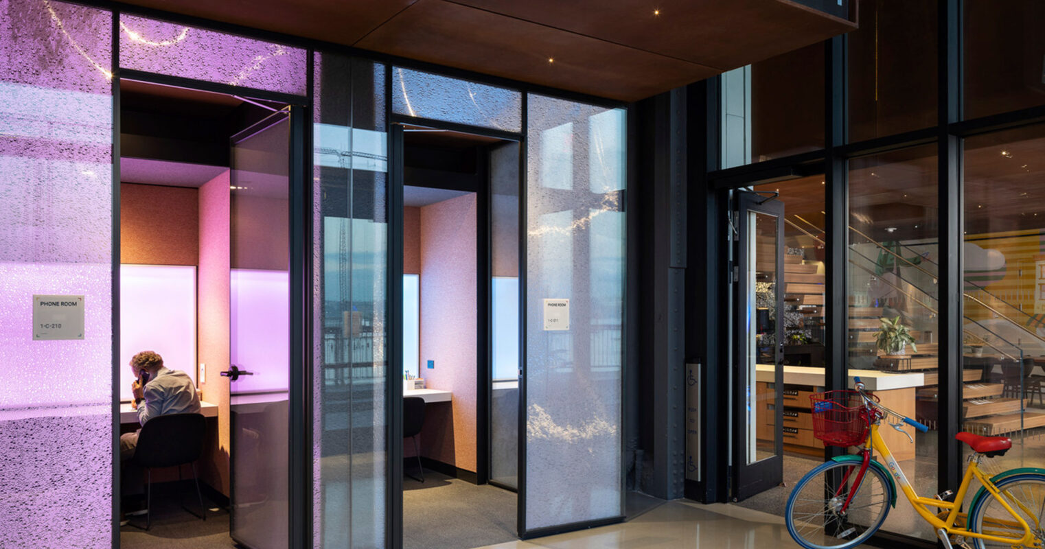 Modern office lobby featuring reflective marble floors, glass partition walls with embedded lighting, and a focal purple illuminated panel. The sleek design includes natural wood tones and a strategically placed yellow bicycle adding a pop of color.