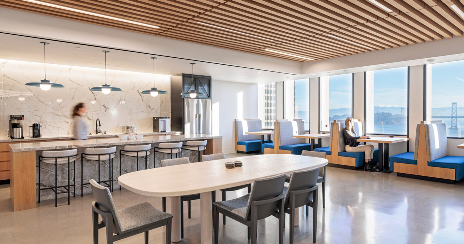 Modern open-plan kitchen and dining space with expansive windows offering natural light, featuring sleek marble backsplash, organic wood slat ceiling, and a combination of pendant lighting and recessed spotlights. Monochrome and blue upholstered banquettes contrast with warm wood tones.